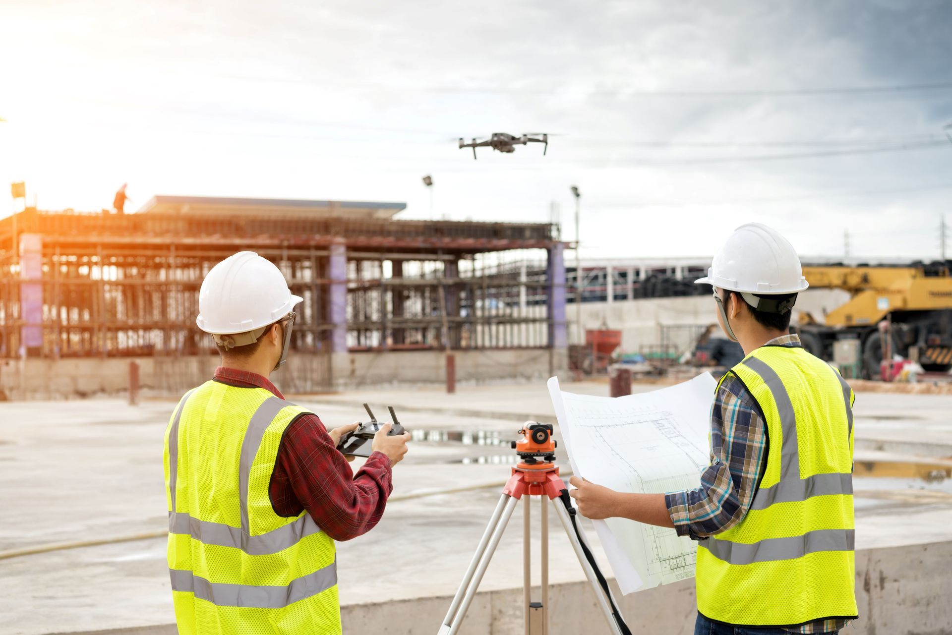 Construction workers in hard hats reviewing plans at a building site with a drone overhead