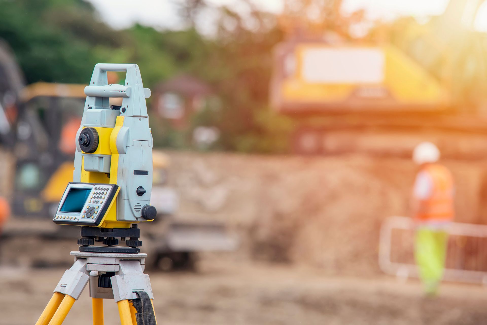 Surveying instrument on tripod at a construction site with workers blurred in the background