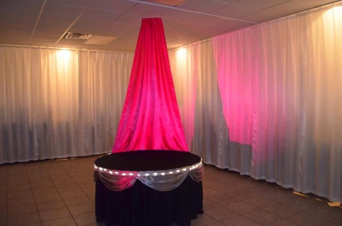 Red draped centerpiece under white ceiling drapes in a softly lit event room