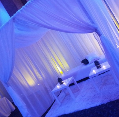 Blue-lit white draped tent with a low table and fluffy rug, creating a cozy lounge setting