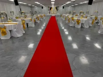Banquet hall with round tables and white chairs, featuring a red carpet aisle down the center.