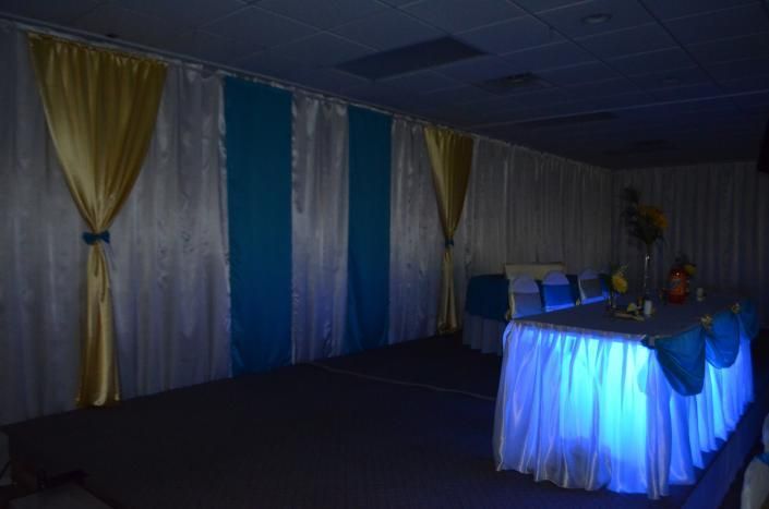 Dimly lit banquet room with blue-draped tables and white-and-gold curtains along the wall