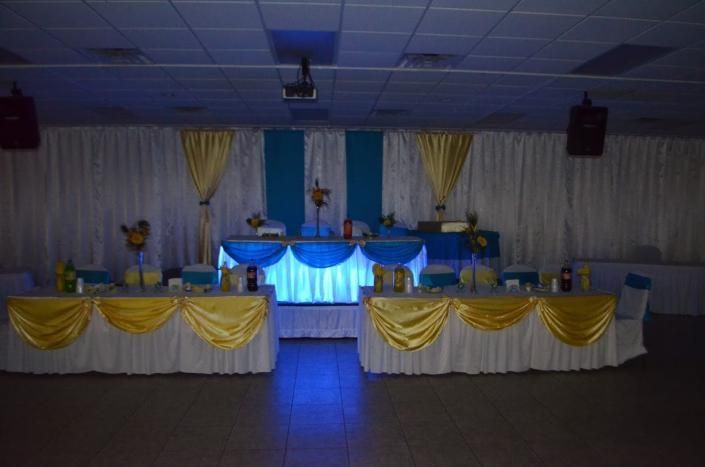 Decorated banquet hall with blue-lit stage and yellow-and-white draped tables