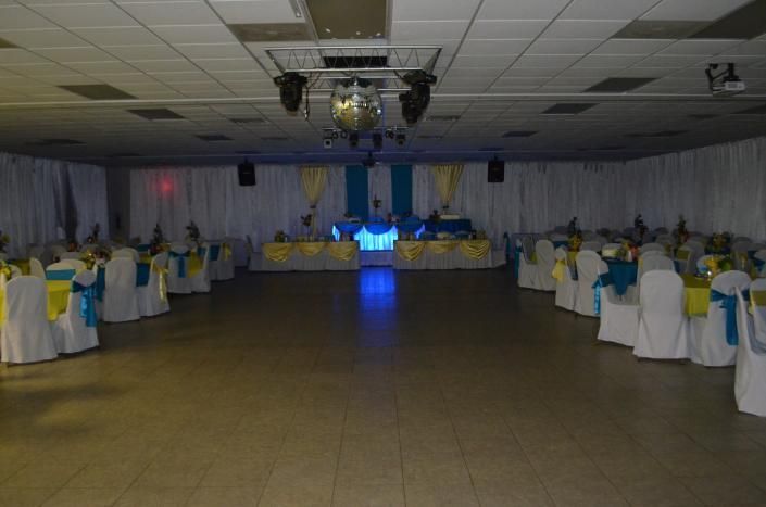 Banquet hall with round tables, white chair covers, blue sashes, and a lit stage at the far end