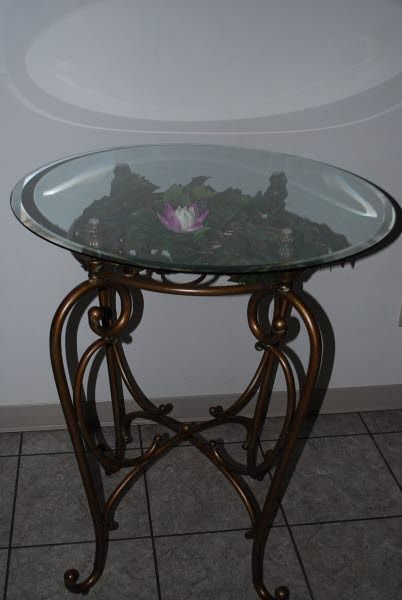 Glass-top decorative table with ornate metal legs and a small flower arrangement underneath