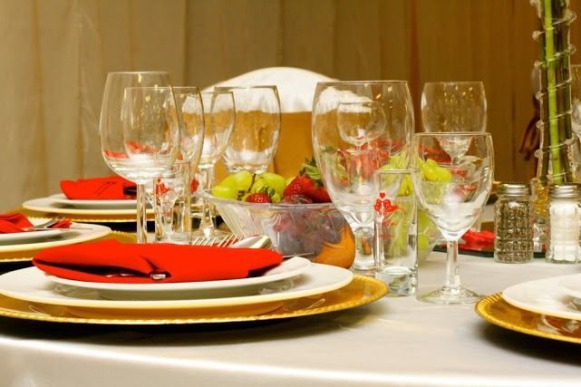 Set dining table with plates, wine glasses, red napkins, and a fruit centerpiece