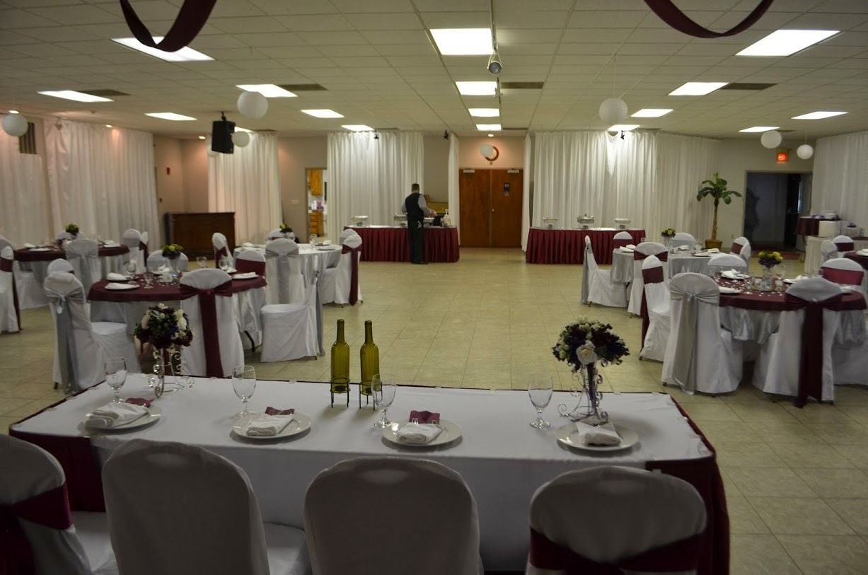 Banquet hall set for a formal event with round tables, white chair covers, and red drapes at the front