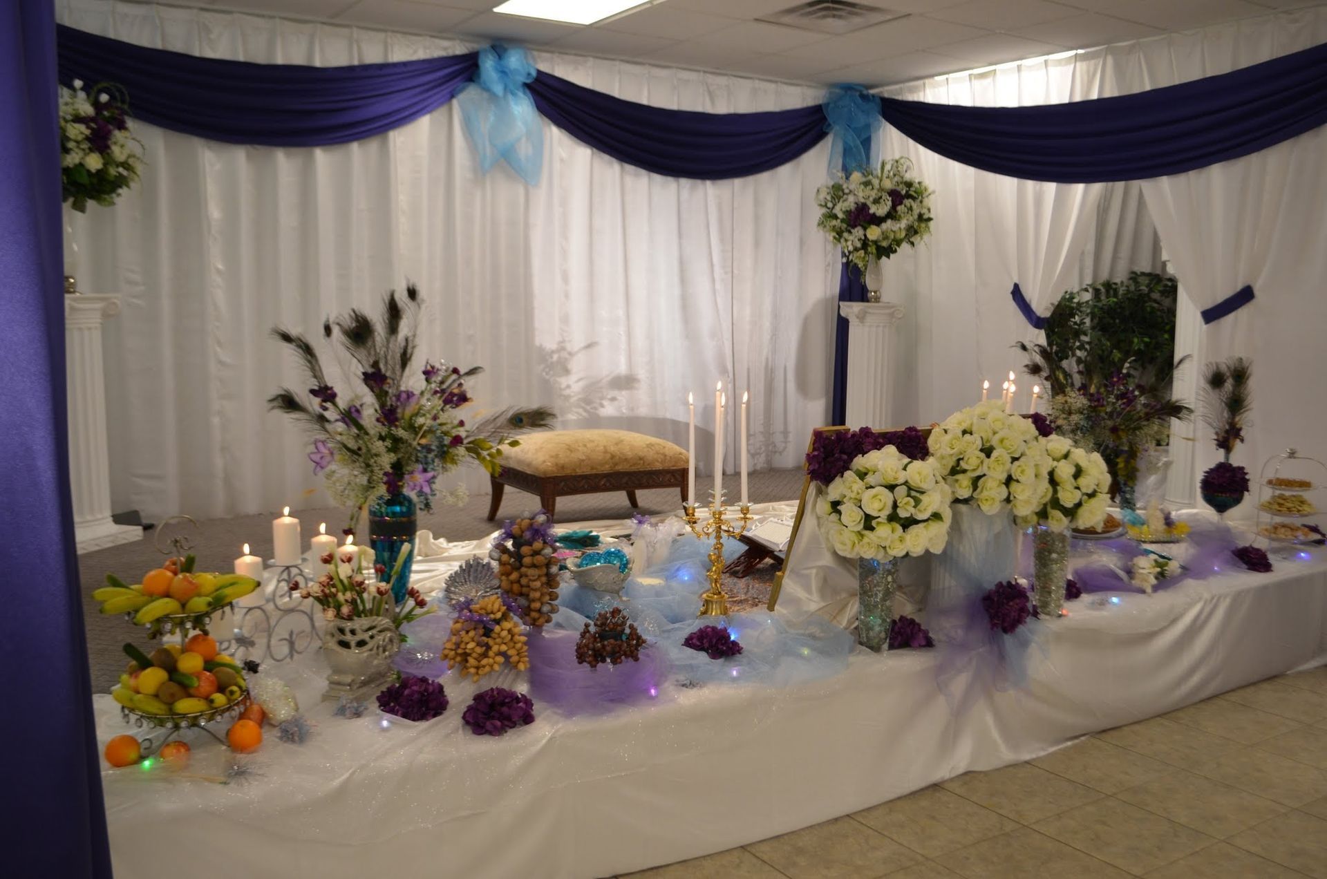 Decorated banquet table with white drapes, purple accents, and floral centerpieces
