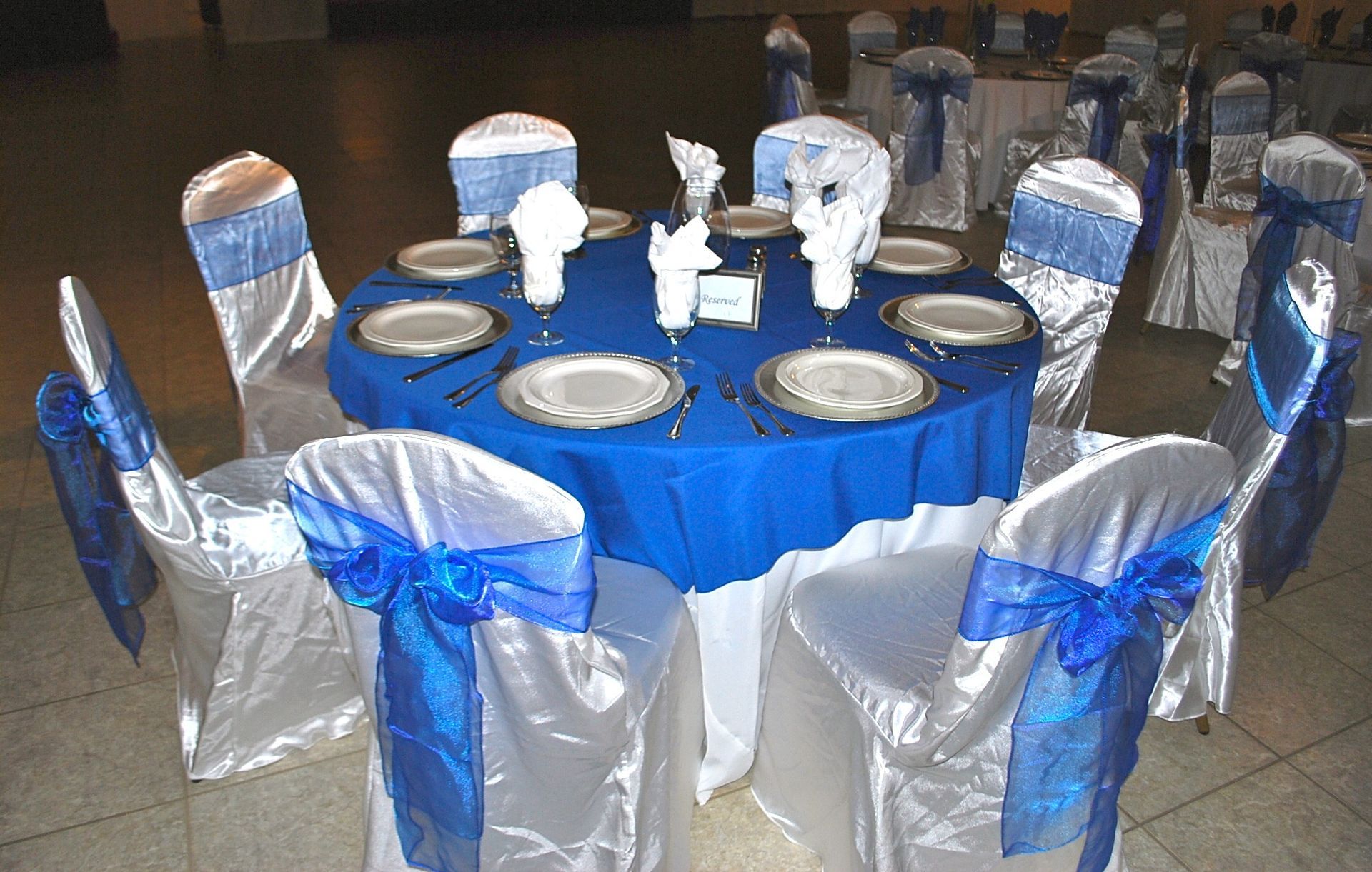Round banquet table with blue tablecloth, silver chair covers, and white centerpieces in a dining hall