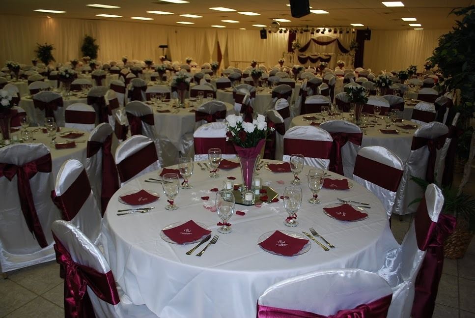Round banquet tables set for an event in a decorated hall with white chair covers and burgundy napkins.