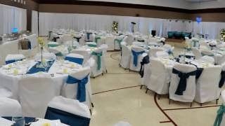 Decorated banquet hall with round tables, white chair covers, and blue sashes set for an event