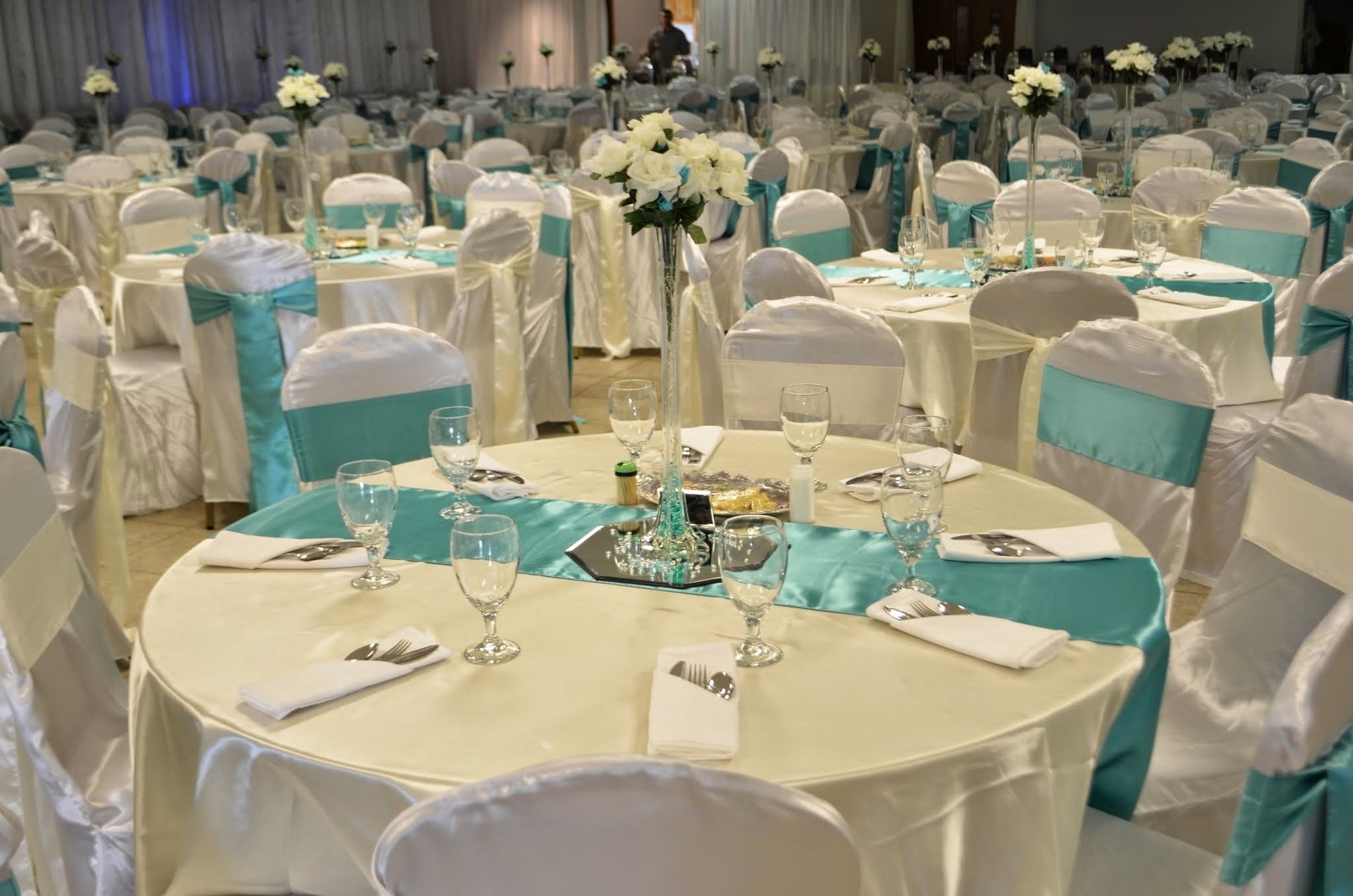 Round banquet tables with white chairs and turquoise accents set in a decorated event hall
