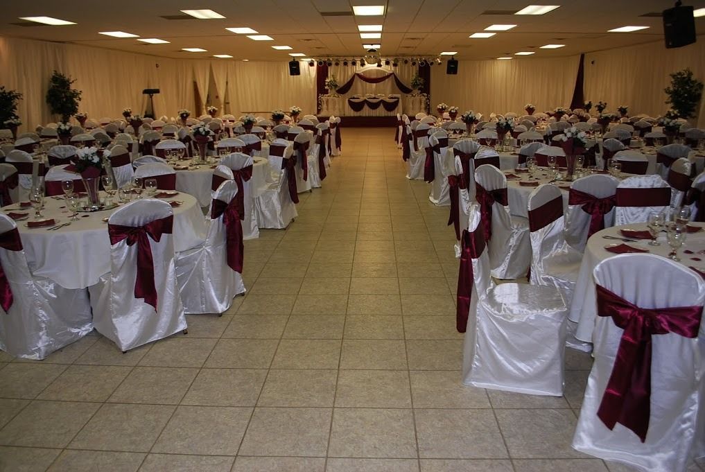 Large banquet hall with rows of white-covered tables and chairs, each tied with burgundy sashes