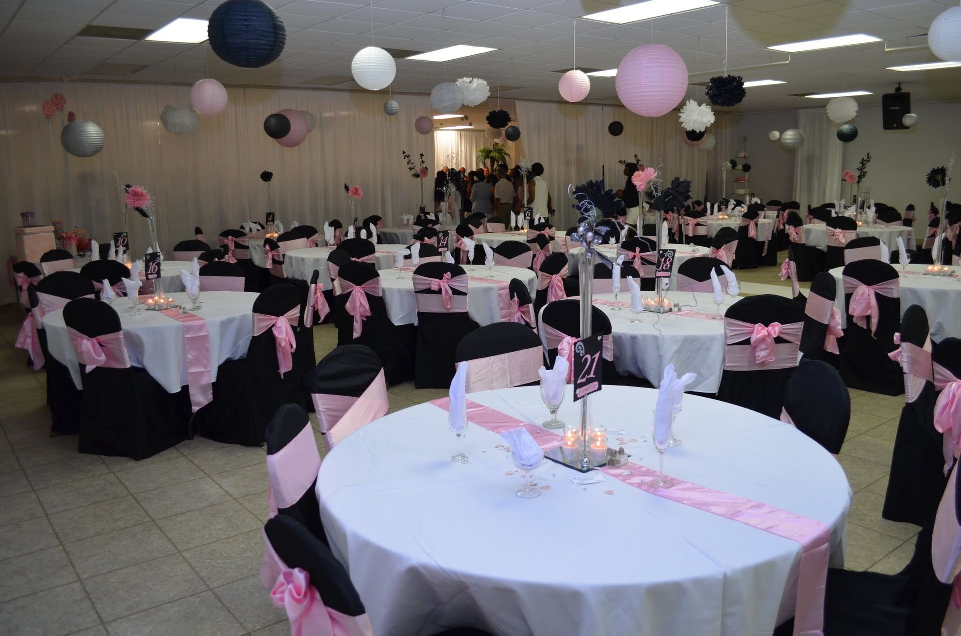 Decorated banquet hall with round tables, pink ribbons, and balloons for a celebration