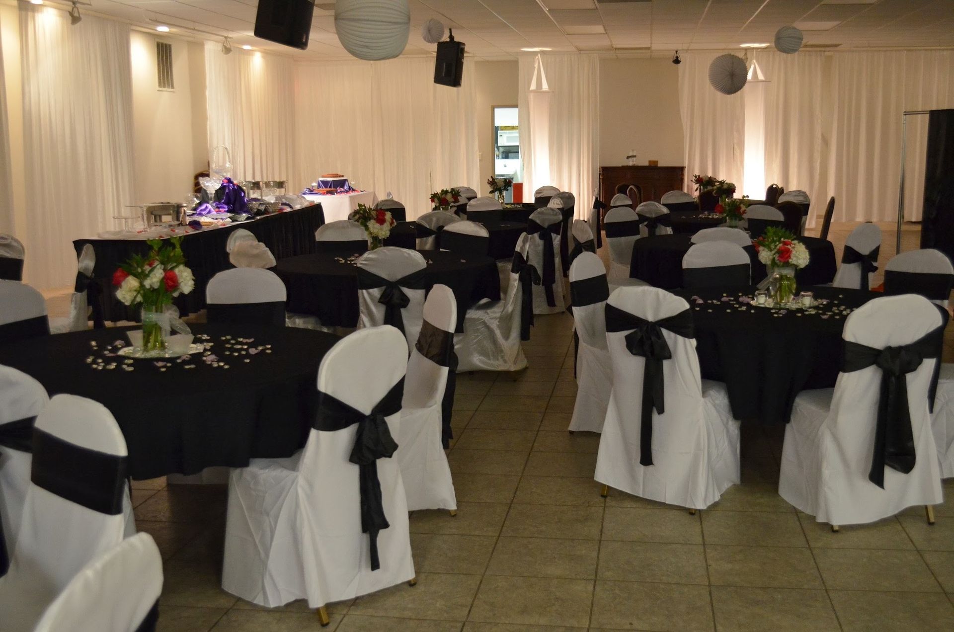 Banquet hall with round tables, black-and-white chair covers, and floral centerpieces set for an event