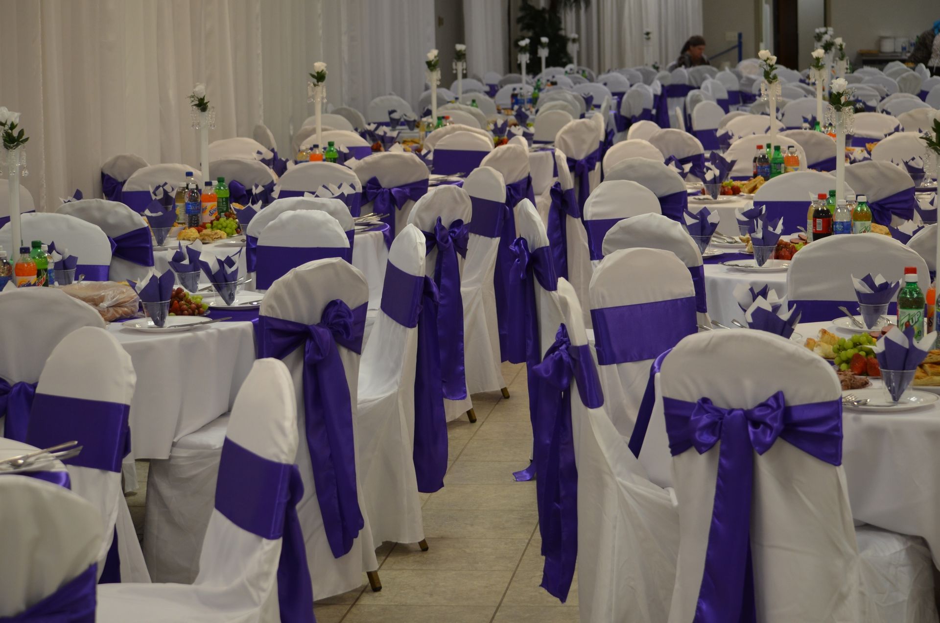 Rows of banquet chairs draped in white and purple bows in a decorated event hall