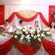 Wedding party seated behind a red-and-white decorated banquet table with floral arrangements