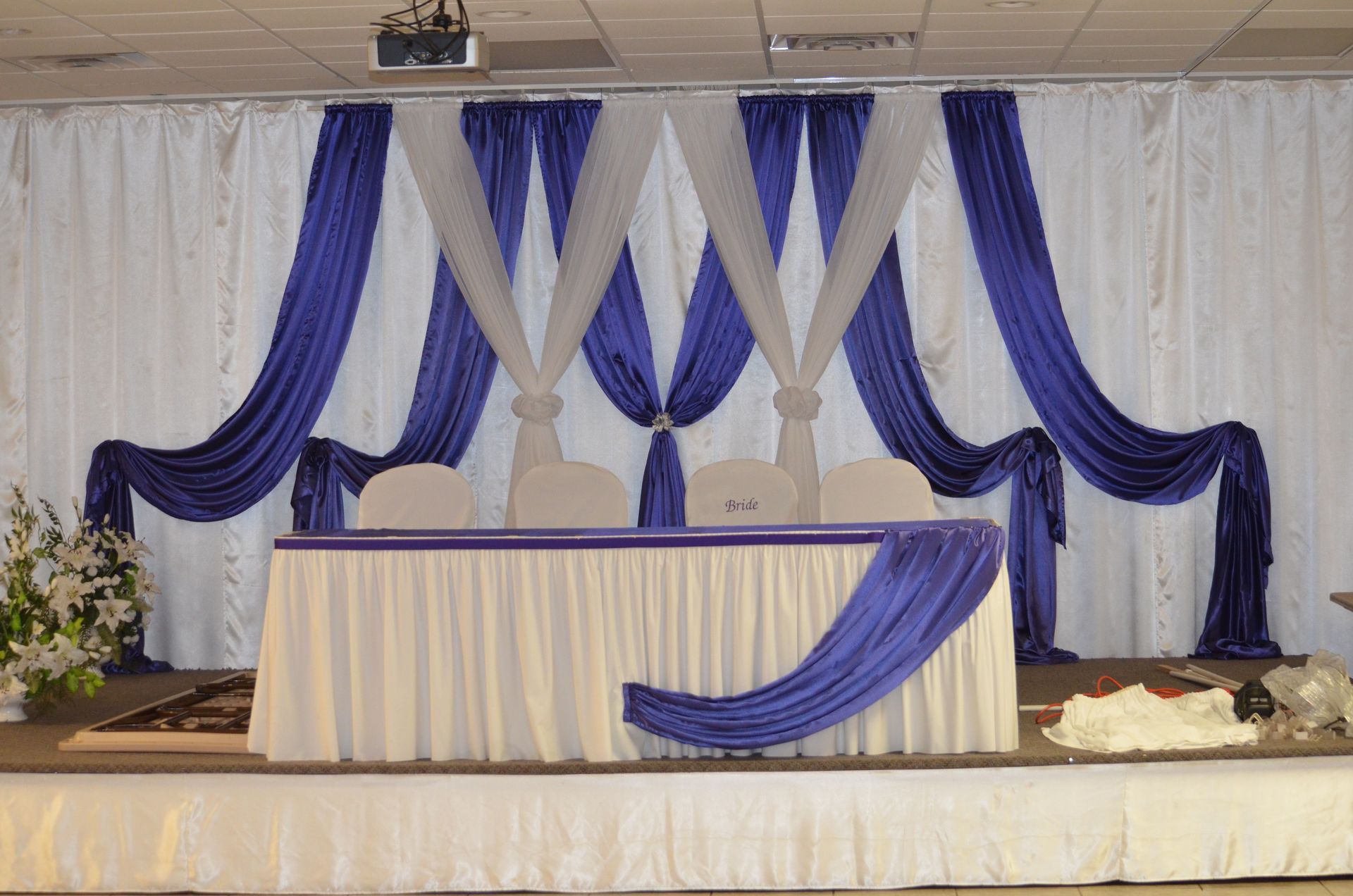 Decorated wedding stage with blue and white drapes, table, and floral arrangements