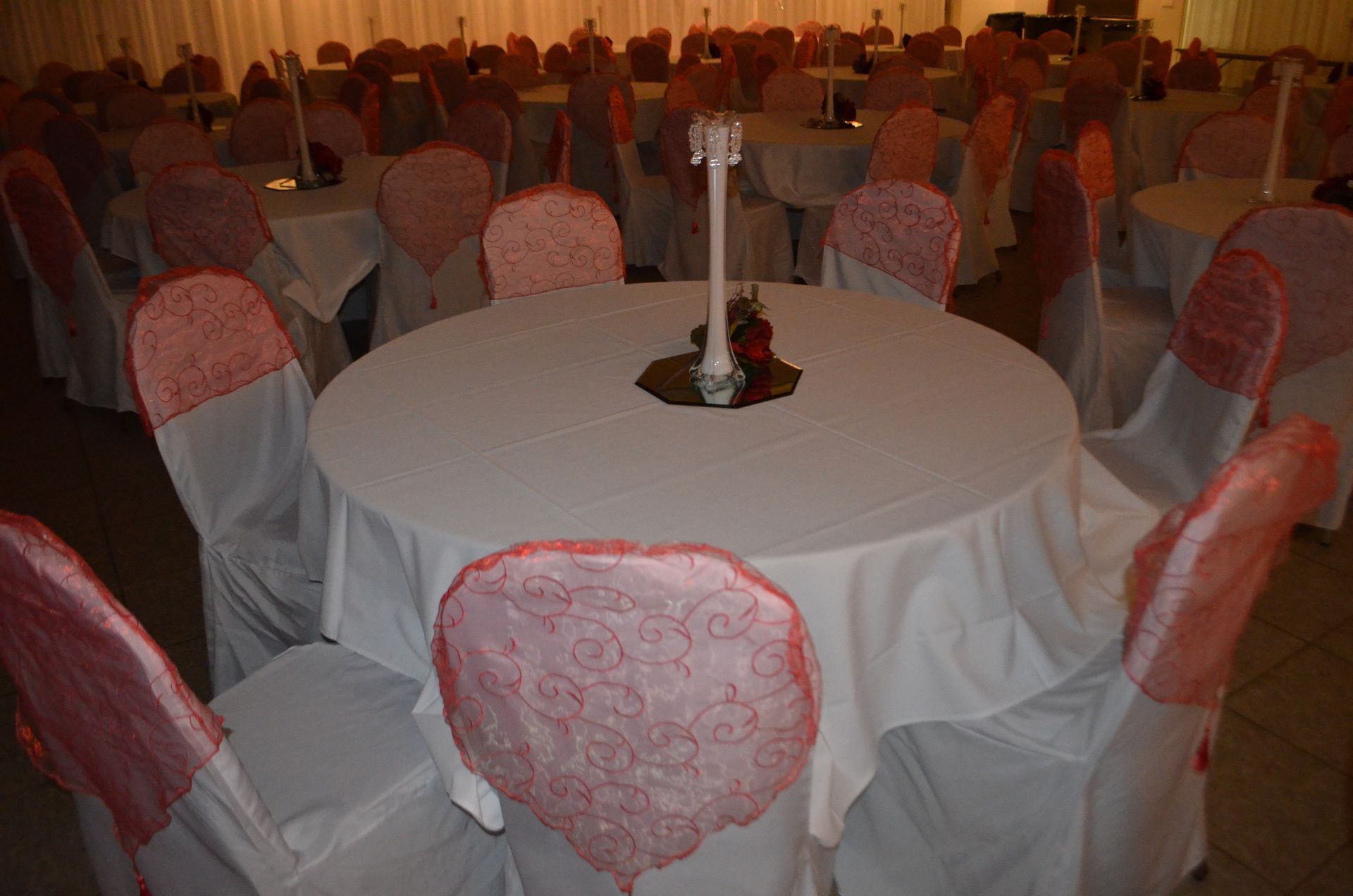 Round banquet table with white cloth and pink chair covers in a warmly lit event hall, surrounded by many empty tables