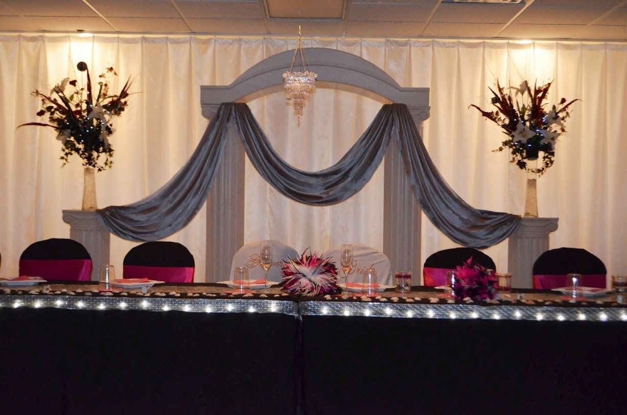 Decorated banquet table with blue drapery, floral arrangements, and a chandelier backdrop