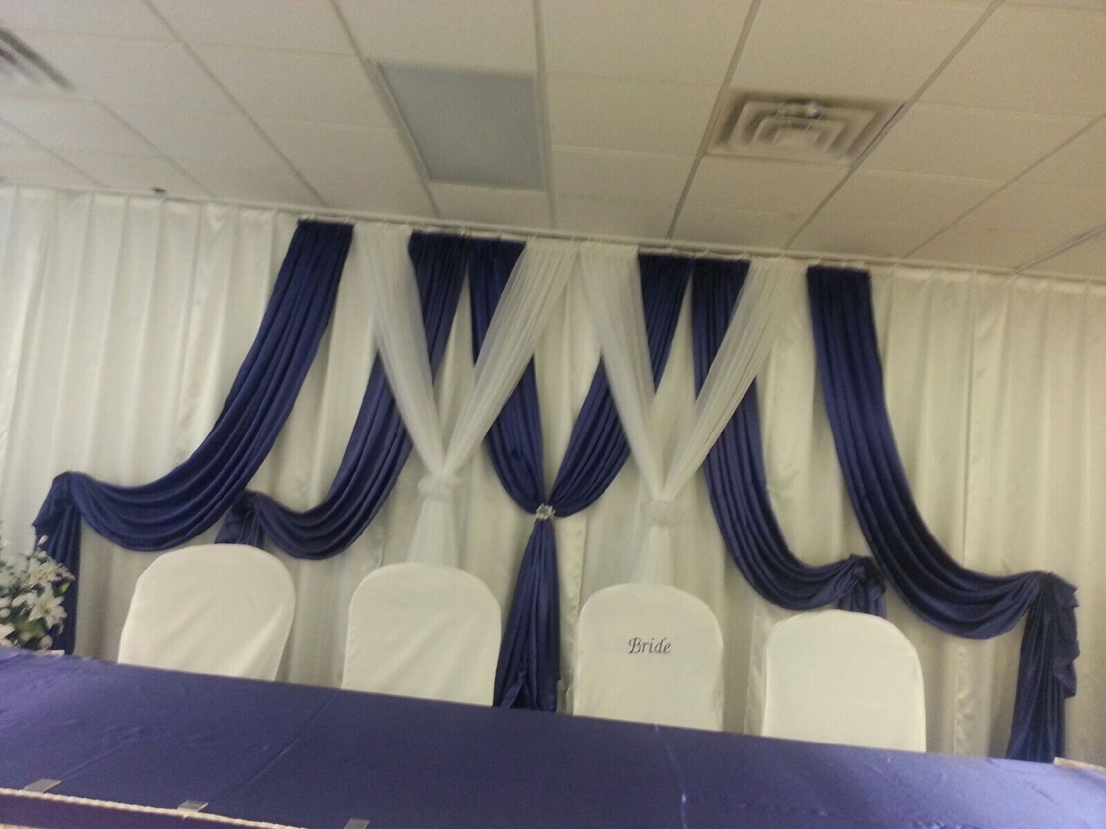 Blue and white draped stage backdrop with four white chairs and a table in front