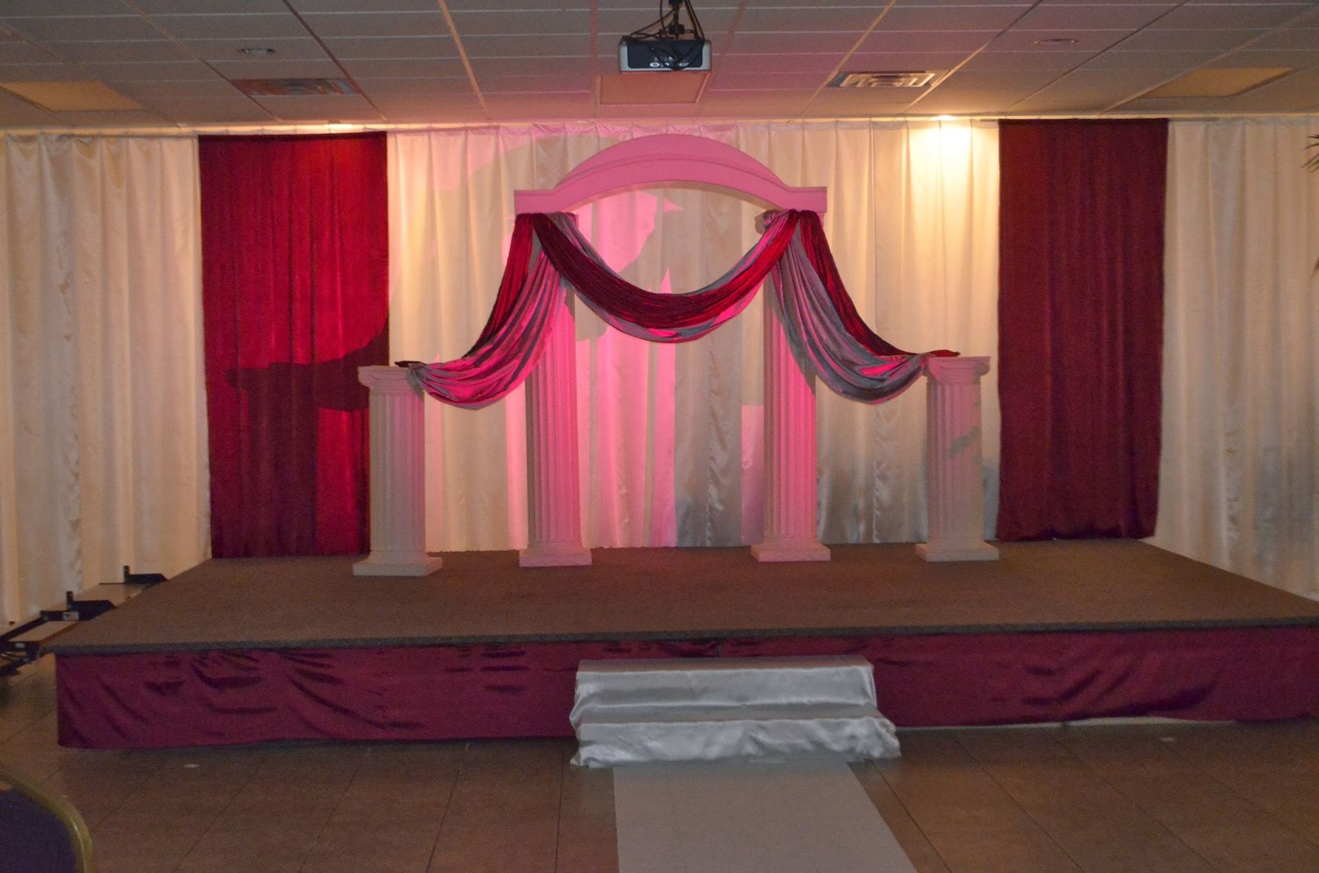 Decorated stage with pink and burgundy drapes and a central staircase in an indoor hall