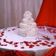 White tiered cake on round table with red rose petals and red draped backdrop