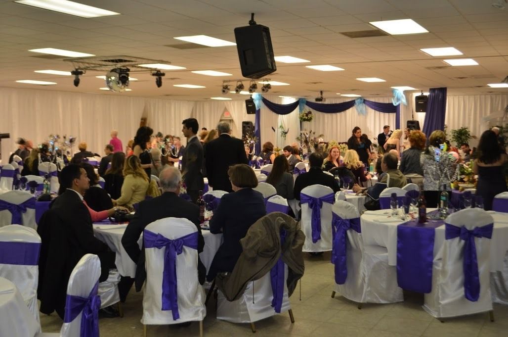 Banquet hall with guests seated at round tables decorated with purple and white chair sashes