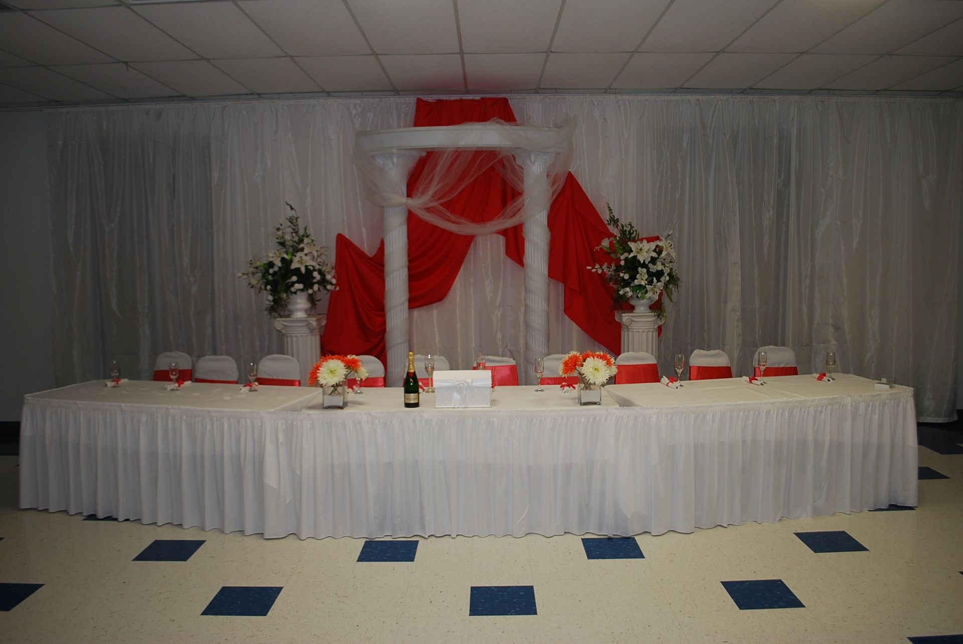Decorated banquet table with white drapes and red accents, set for an event or wedding reception