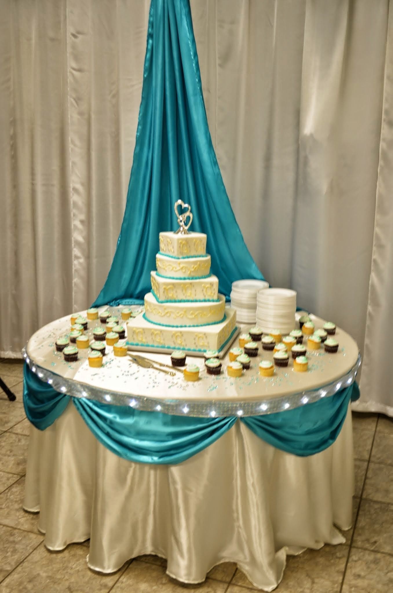 Tiered white cake on a draped table with teal and cream decor at a formal event