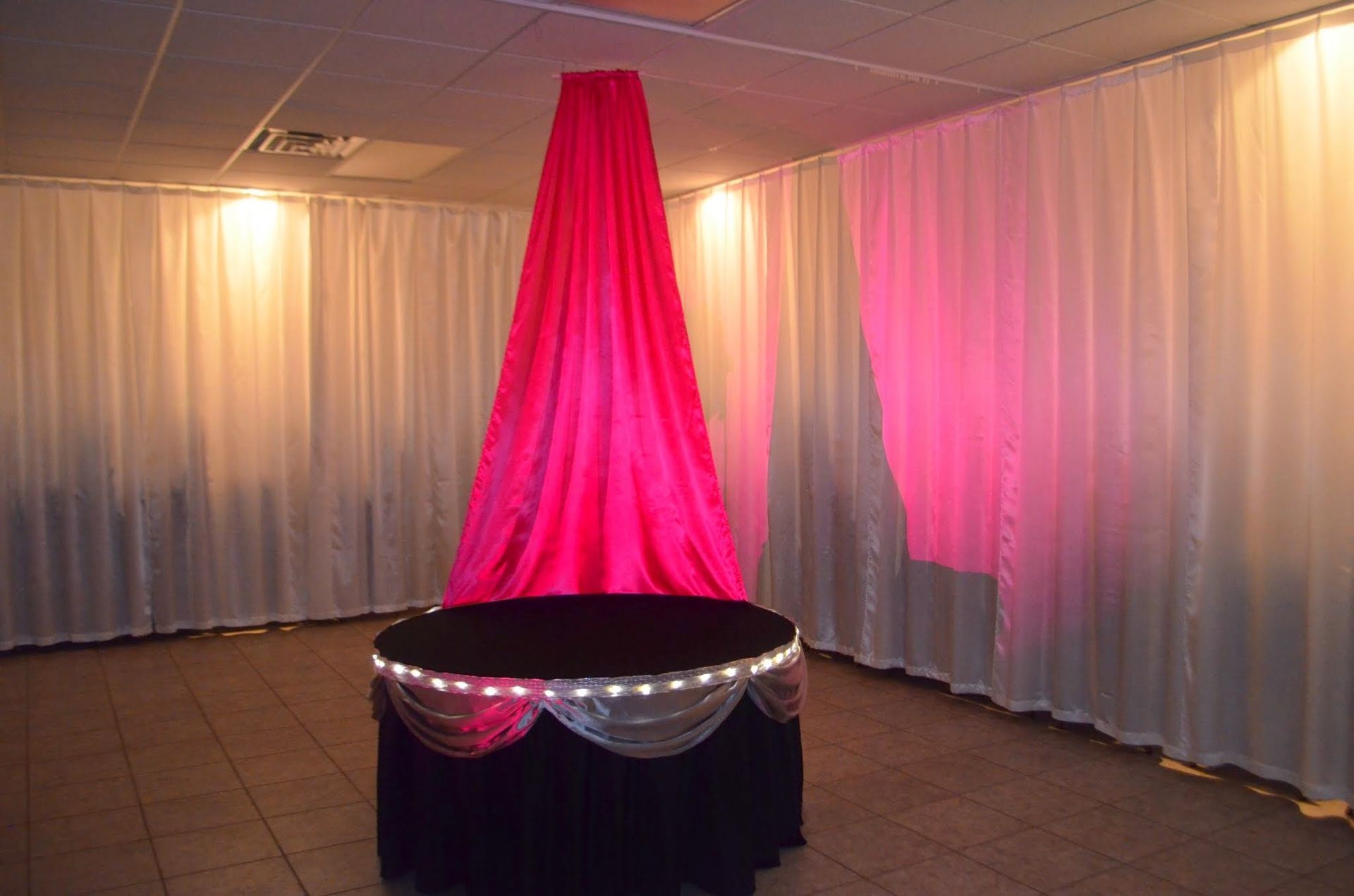 Pink-lit draped event display with a round black table and white curtains in a banquet room