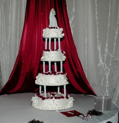 White tiered cake display with red draped backdrop and small table decor