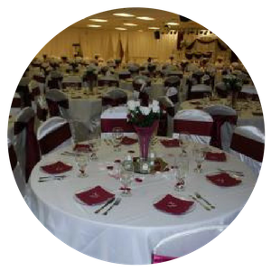 Banquet hall with round tables set with white tablecloths and burgundy napkins, viewed from a foreground table