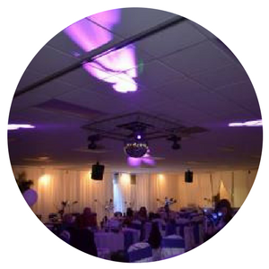 Circular photo of a banquet hall with purple lighting, round tables, and a mirrored disco ball ceiling centerpiece