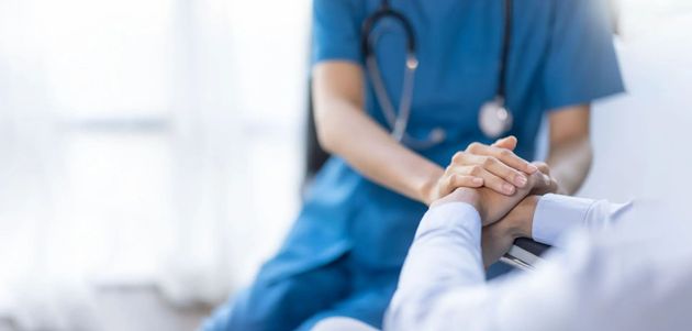 Nurse in blue scrubs holding a patient’s hand in a hospital setting Nurse in blue scrubs holding a patient’s hand in a hospital setting