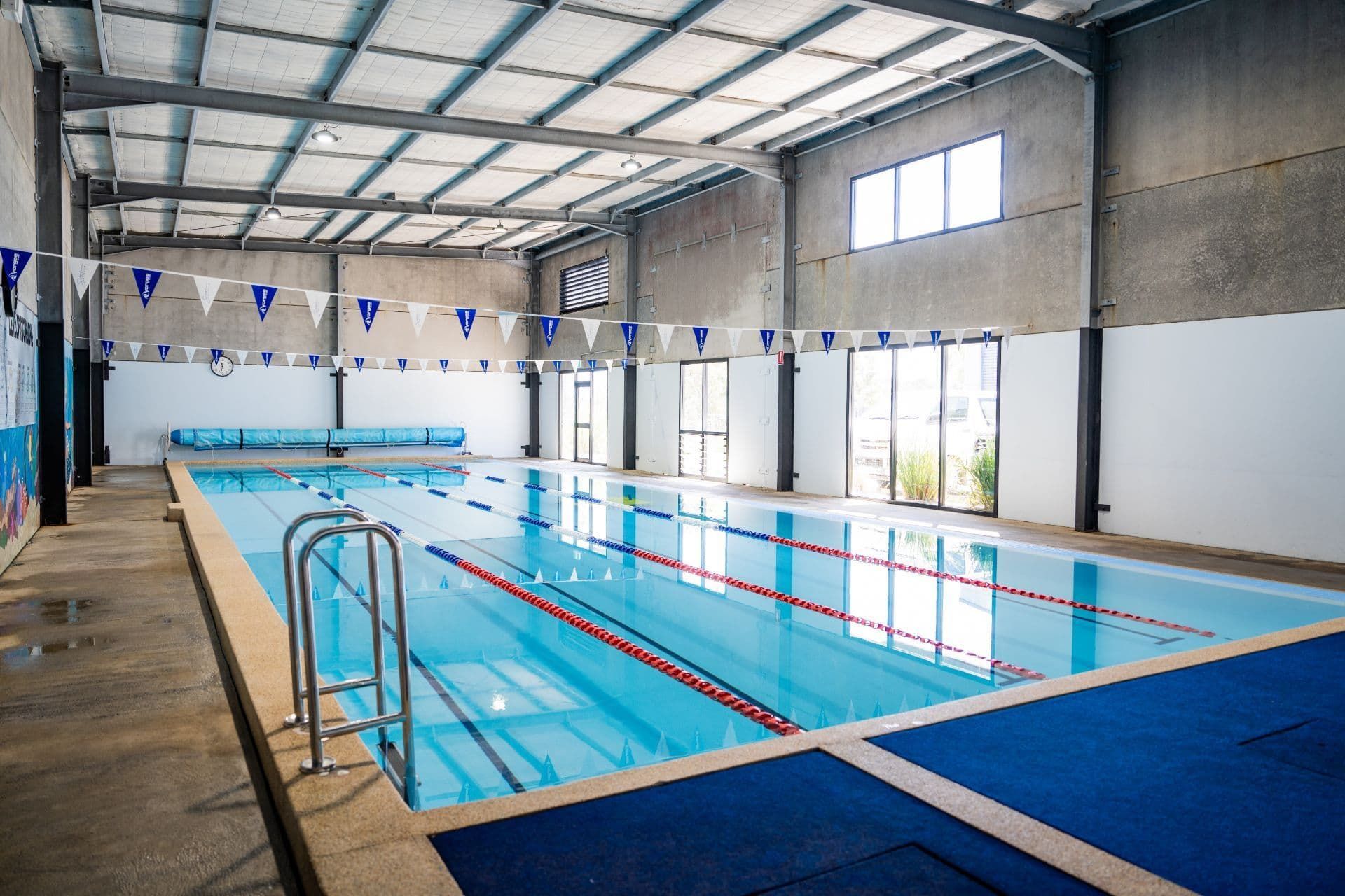 A large indoor swimming pool with blue flags hanging from the ceiling — North Wyong Aqua Centre In Wyong, NSW