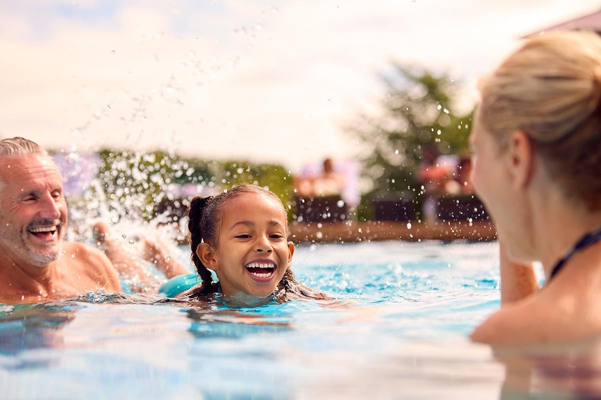 Teaching Granddaughter To Swim On Family Summer Holiday In Pool
