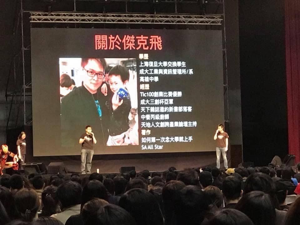 A group of people are standing in front of a large screen with chinese writing on it