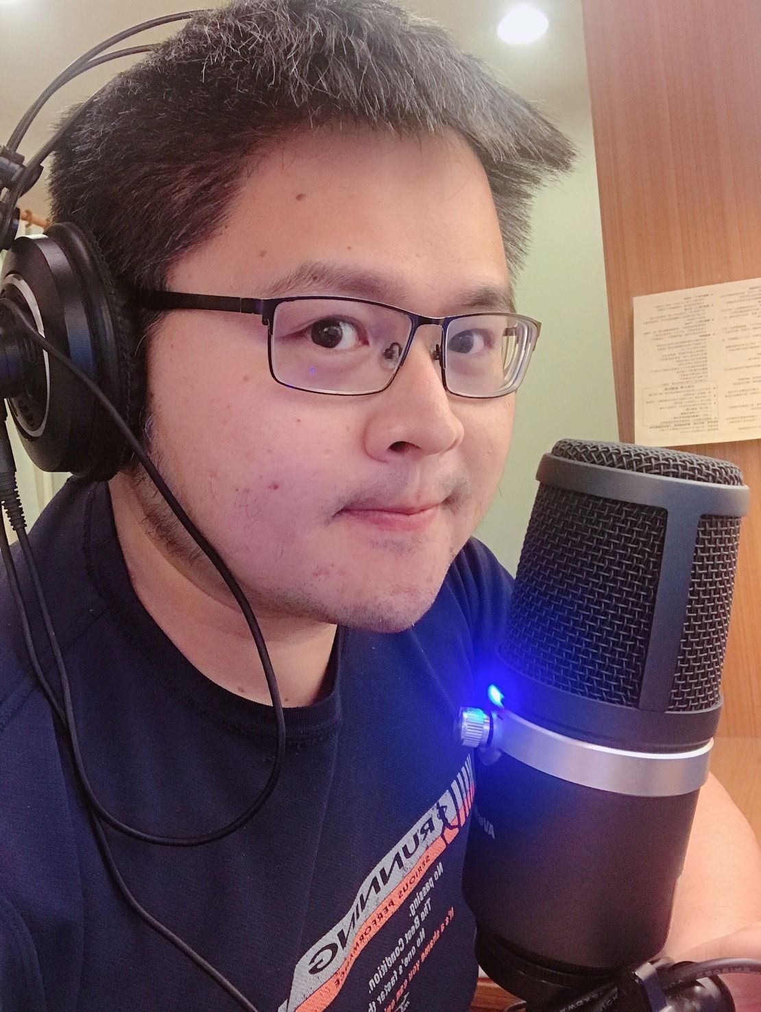 A man wearing glasses and headphones is standing in front of a microphone.