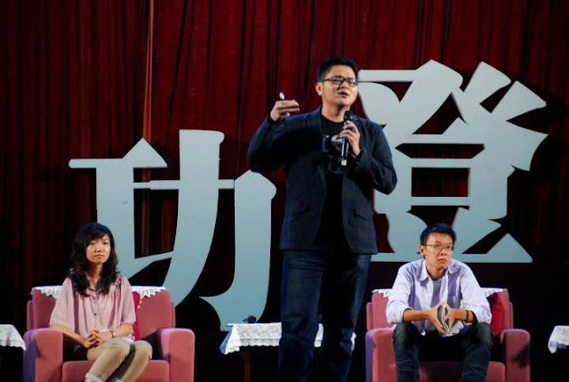 A man is speaking into a microphone in front of chinese characters