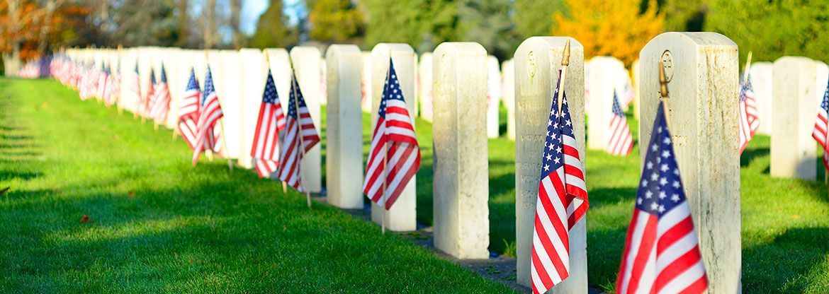 White gravestones in a row with small American flags in a cemetery lawn