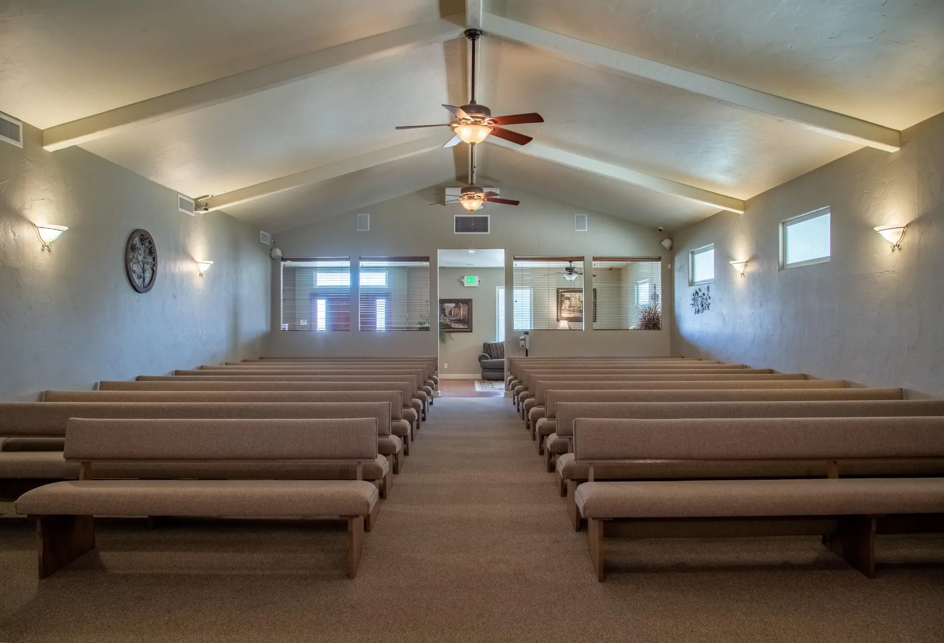 Empty church interior with pews, white walls, and ceiling fans leading to a front entrance