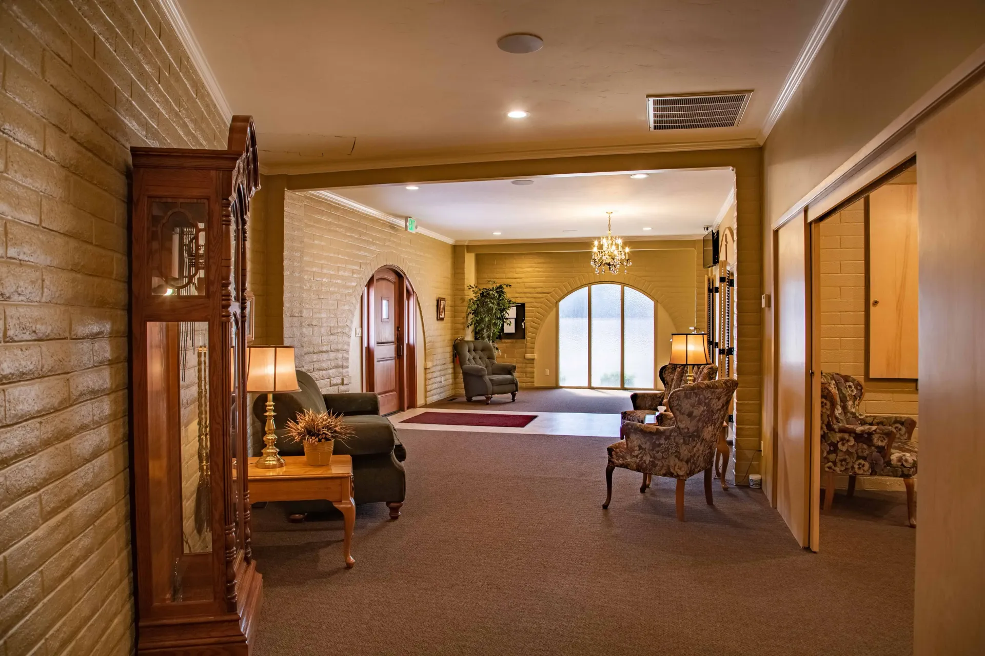 Warm hotel hallway with carpet, wooden trim, and a bright lounge area at the end