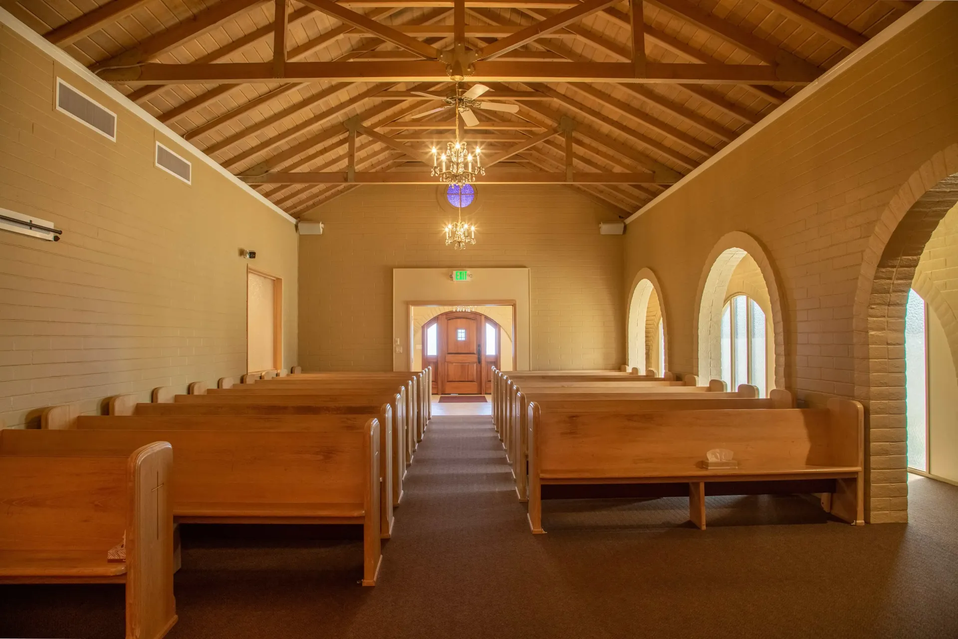 Empty church interior with wooden pews, arched windows, and exposed beam ceiling