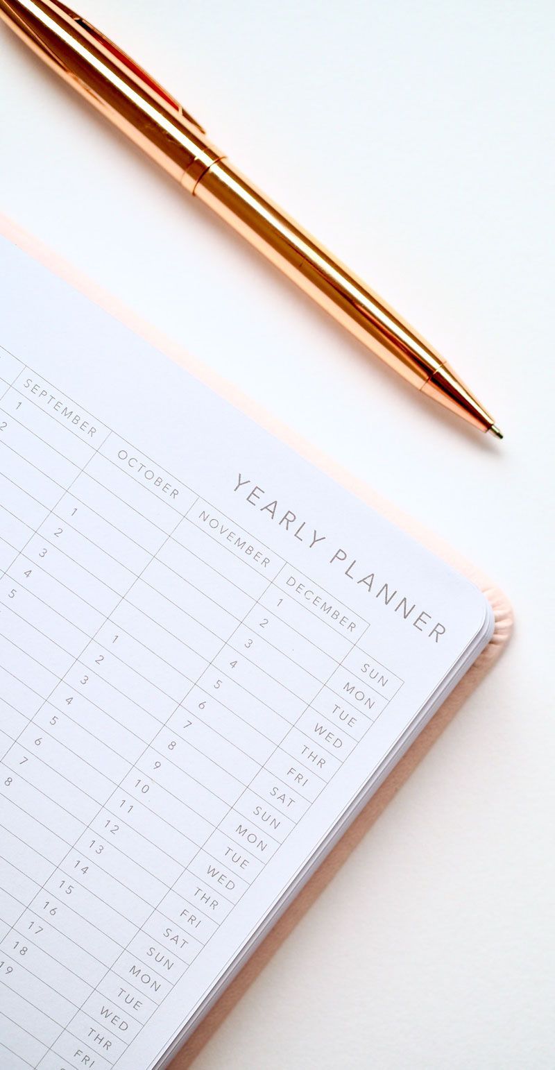 Rose gold pen beside a white weekly planner on a light background