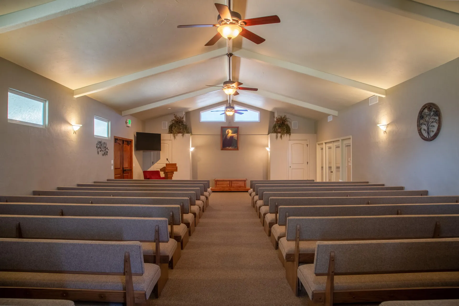 Small church sanctuary with rows of pews, a central aisle, ceiling fans, and a pulpit at the front