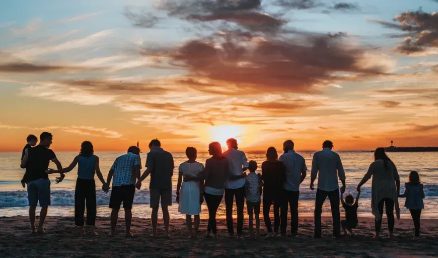 Group standing on a beach at sunset, silhouetted against a colorful orange-blue sky.