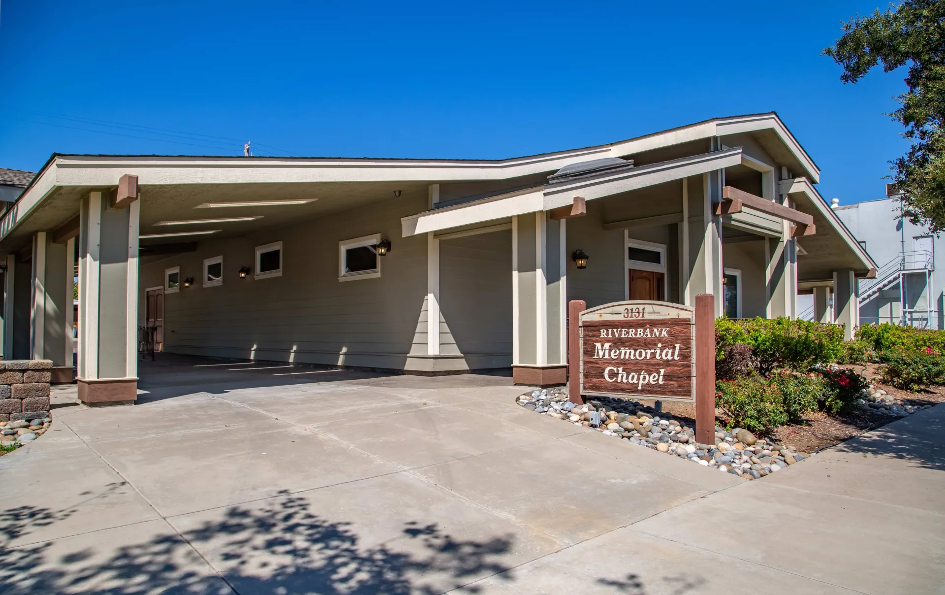 Exterior of a beige building with a covered entrance, driveway, and stone sign under a clear blue sky
