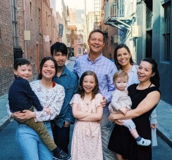 Smiling family of six standing together in a narrow city alleyway
