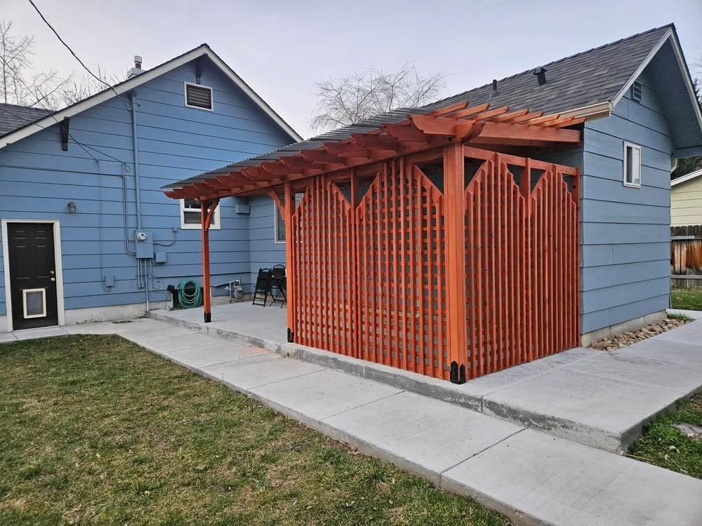 Orange wood pergola attached to a blue house beside a concrete walkway in a yard